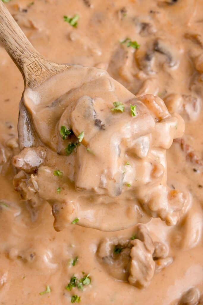 Close up view of beef stroganoff garnished with parsley on a spoon.