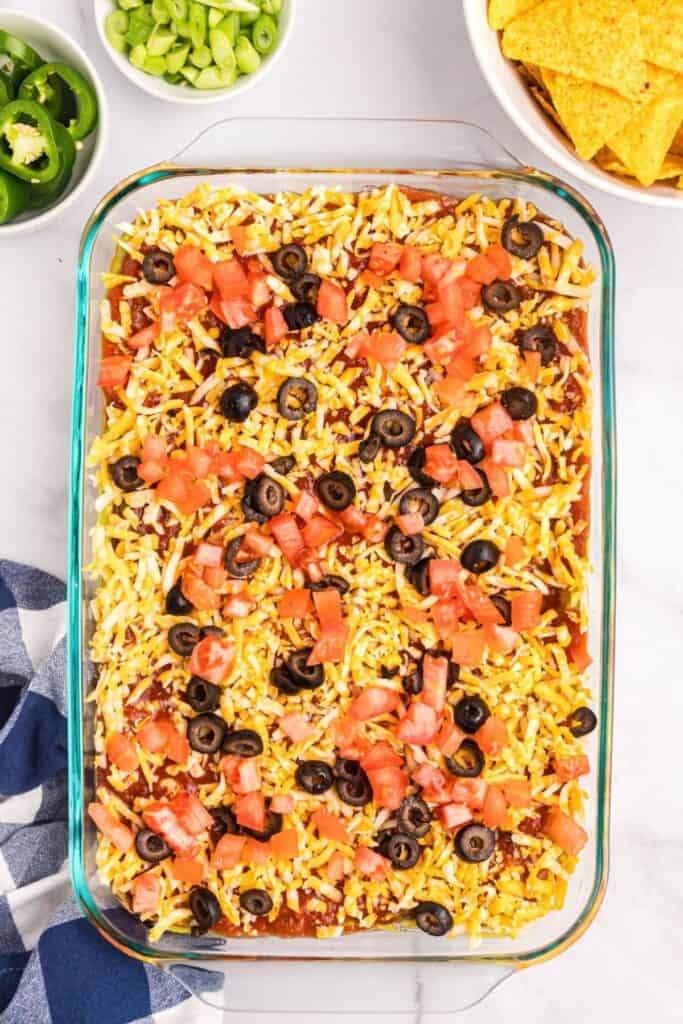 Top 7 layer dip with shredded cheese, tomatoes, and black olives.