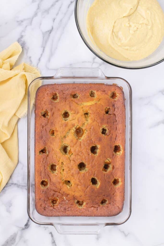 Cake with holes poked into the top. Prepared banana pudding in a bowl above.