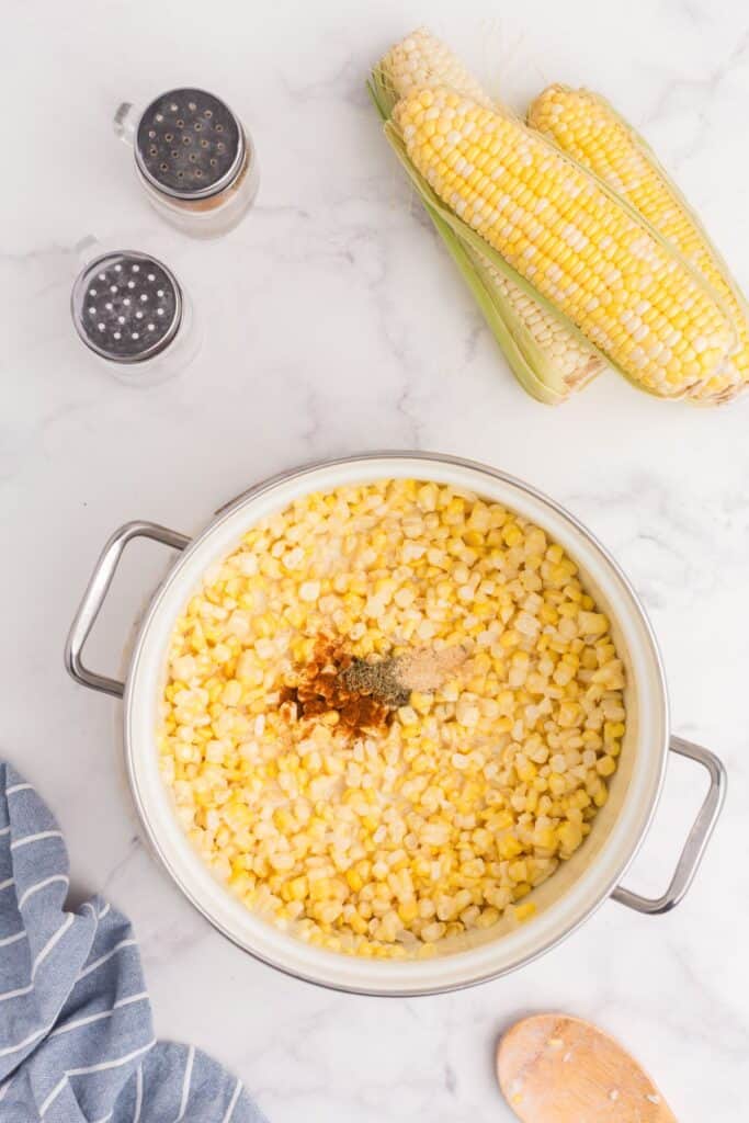 Creamed corn during cooking process with spices added to the center of the pot.