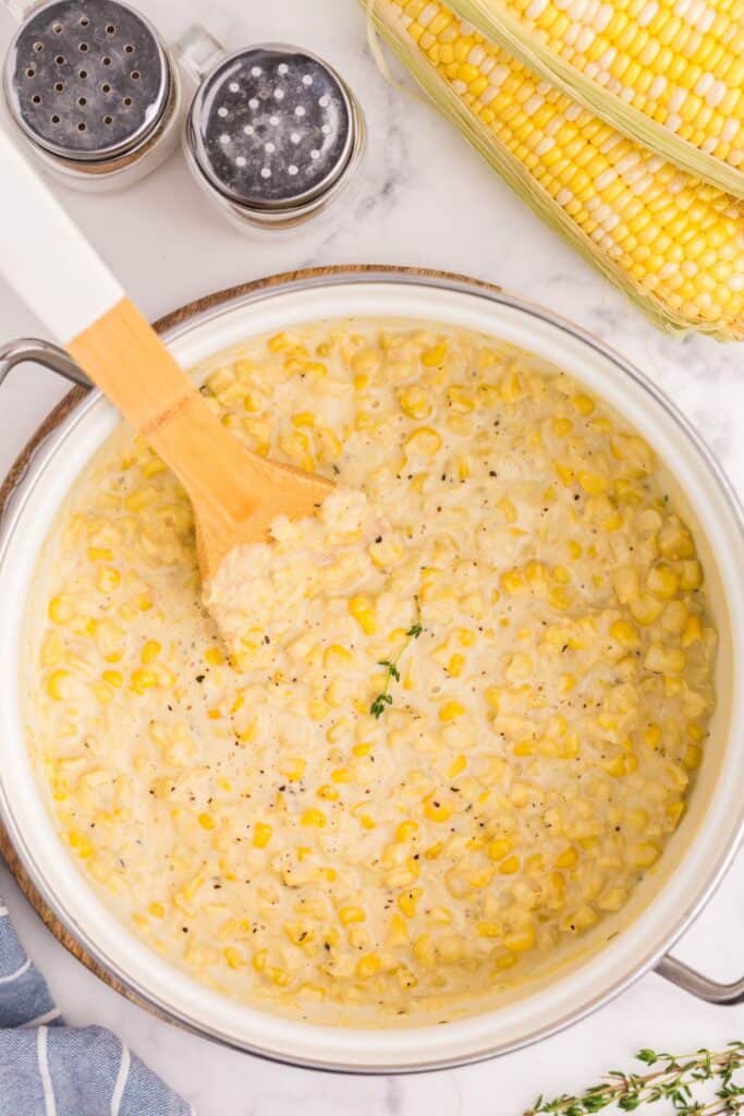 Completed and garnished creamed corn with a wooden spoon in the cooking pot.