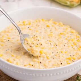 White serving bowl of creamed corn with a silver serving spoon.