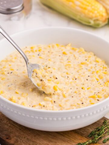 White serving bowl of creamed corn with a silver serving spoon.