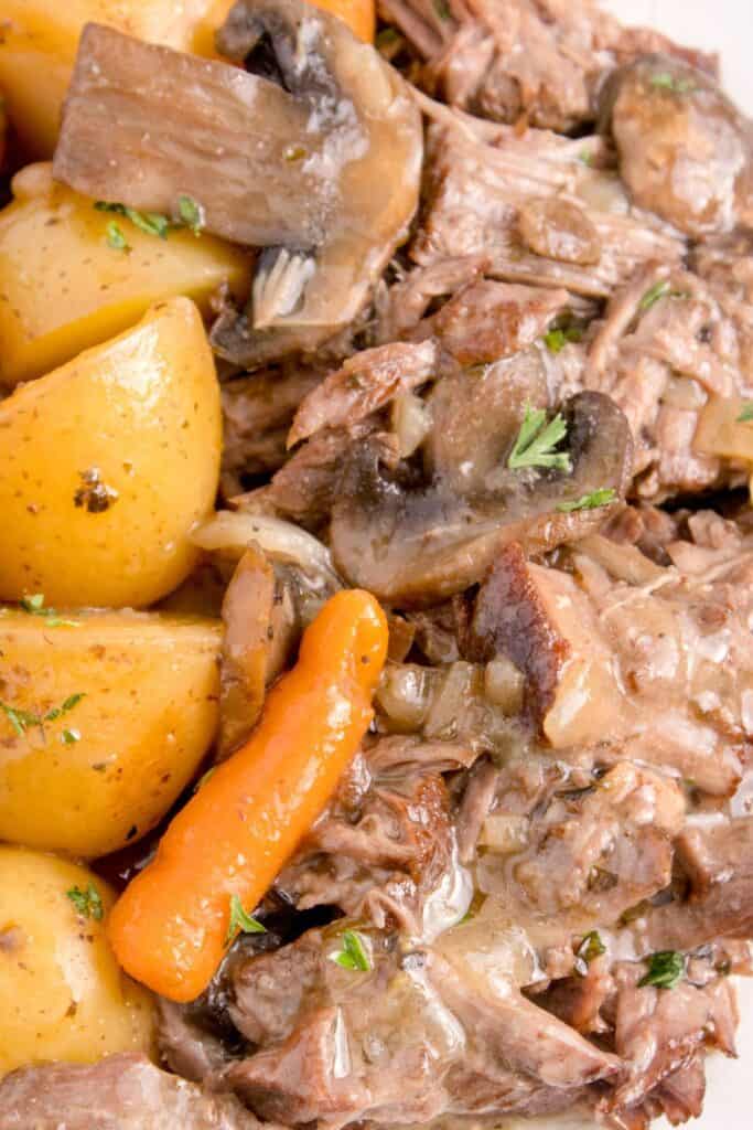 Close up view of chuck roast with carrots, potatoes, and mushrooms on a white plate