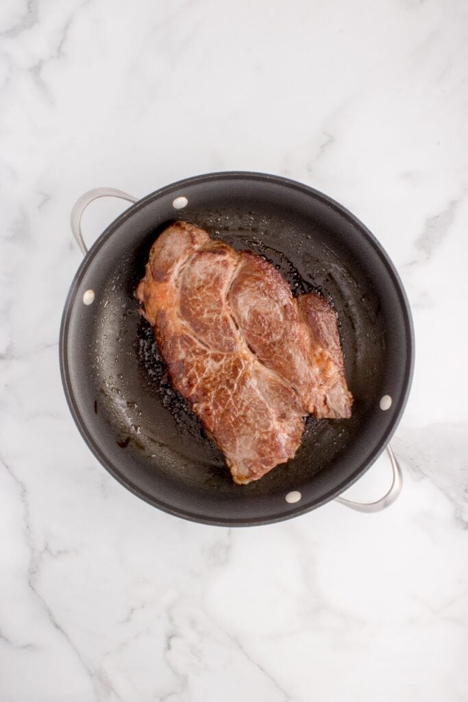 Seared chuck roast in a large pan.