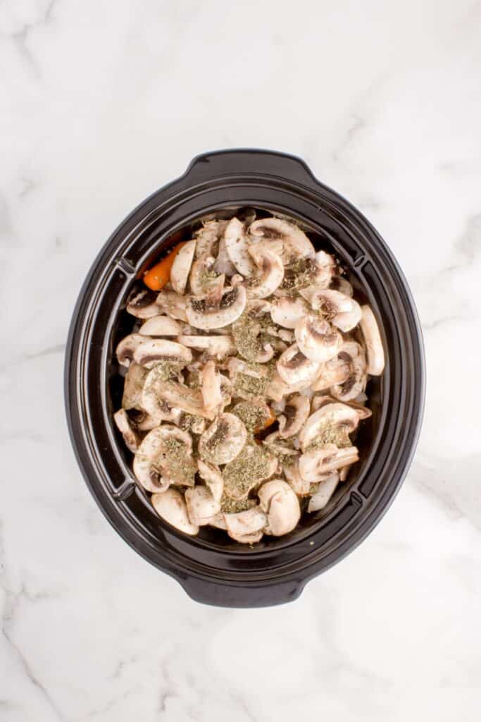 Chuck roast recipe with raw vegetables layered on top in slow cooker insert.