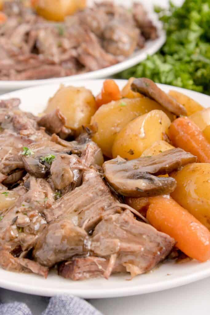 Large portion of chuck roast with potatoes, carrots, and mushrooms on a white plate.