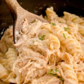 Garlic Parmesan Chicken and Pasta in a slow cooker with a wooden spoon