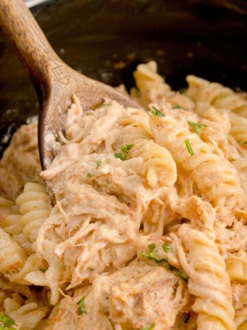 Garlic Parmesan Chicken and Pasta in a slow cooker with a wooden spoon