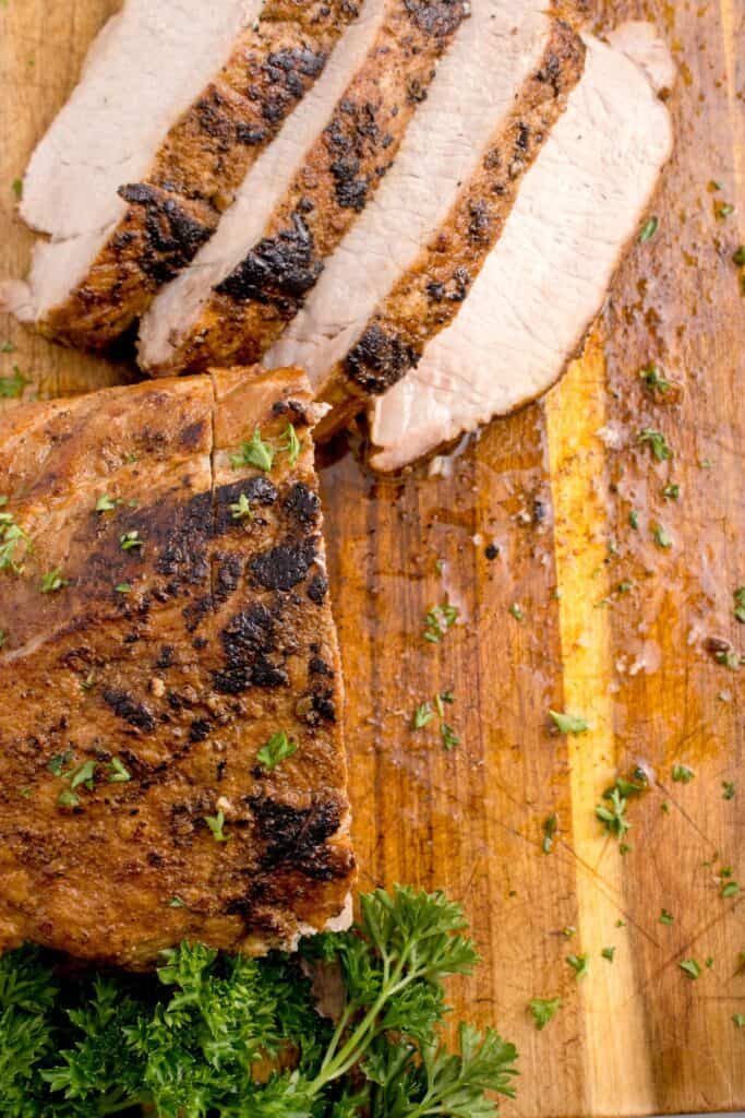 Overhead shot of pork tenderloin partially sliced on a large cutting board.