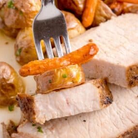 Sliced Instant Pot pork loin on a white plate with carrots and potatoes. A silver fork is loaded with a bite of each.