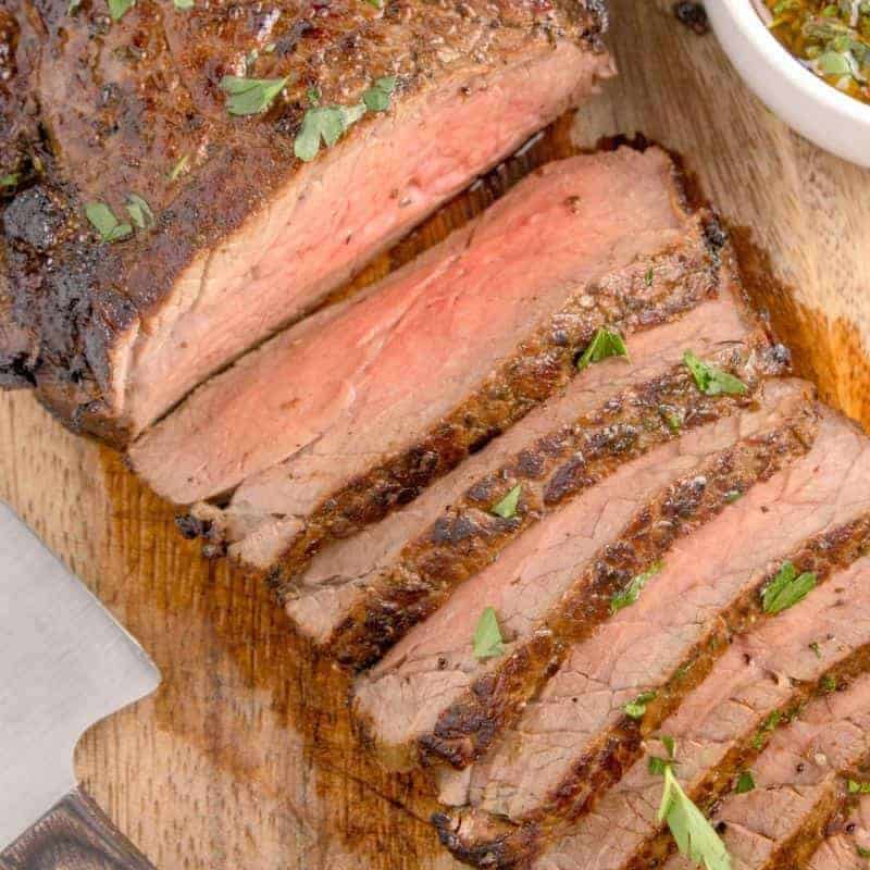 Sliced london broil beef sprinkled with herbs on cutting board.