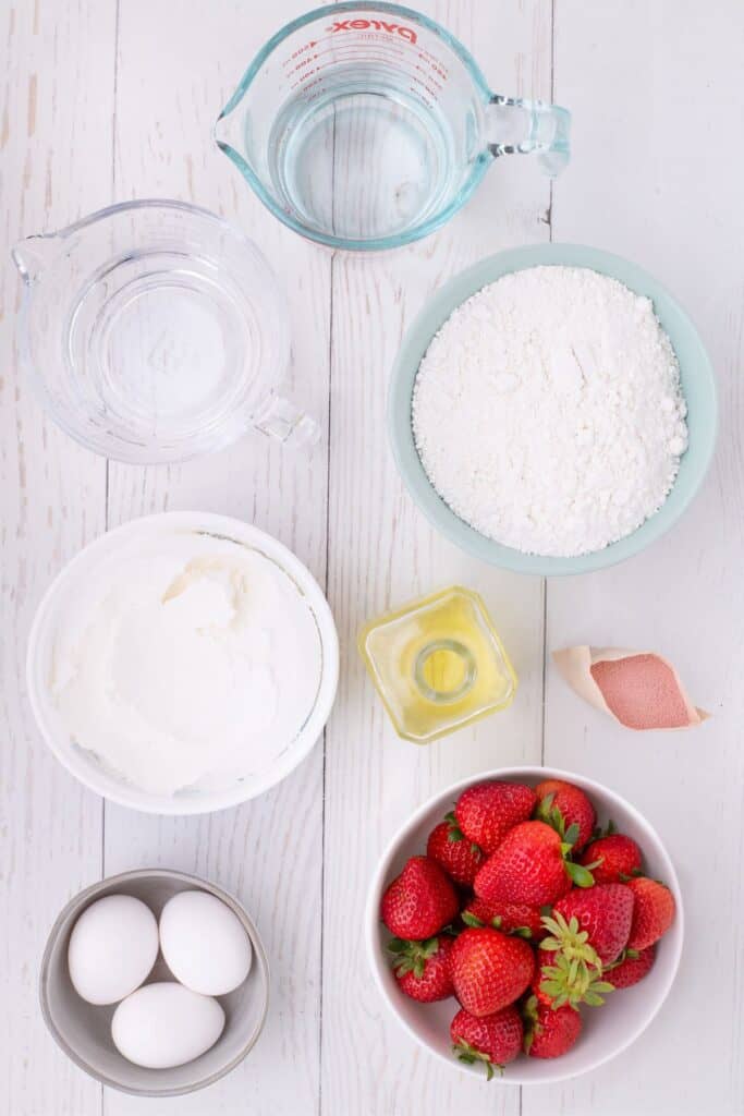 Ingredients needed for strawberry jello cake: water, white box cake mix, vegetable oil, strawberry jello packet, fresh strawberries, eggs, cool whip, and boiling water (for jello).