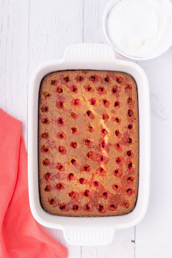 Baked strawberry jello cake with holes poked through, and jello mix poured over the top.