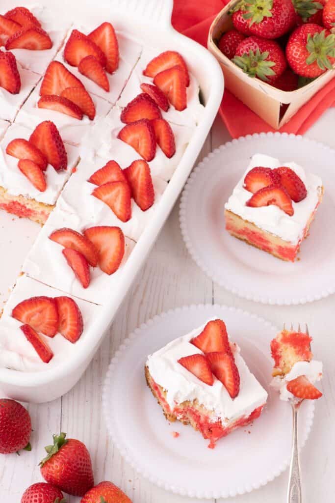 Completed and sliced strawberry jello cake. Two pieces on white plates to the right of image.