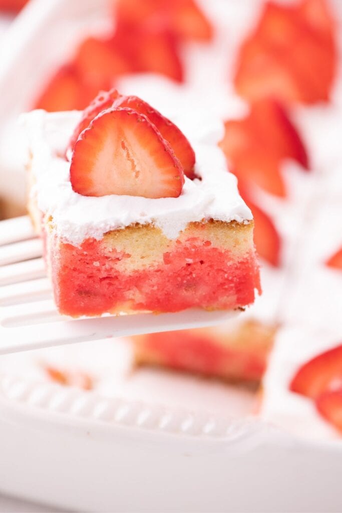 Slice of strawberry jello cake on spatula in foreground.