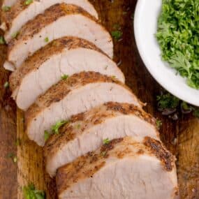 oven baked pork tenderloin sliced on a cutting board.