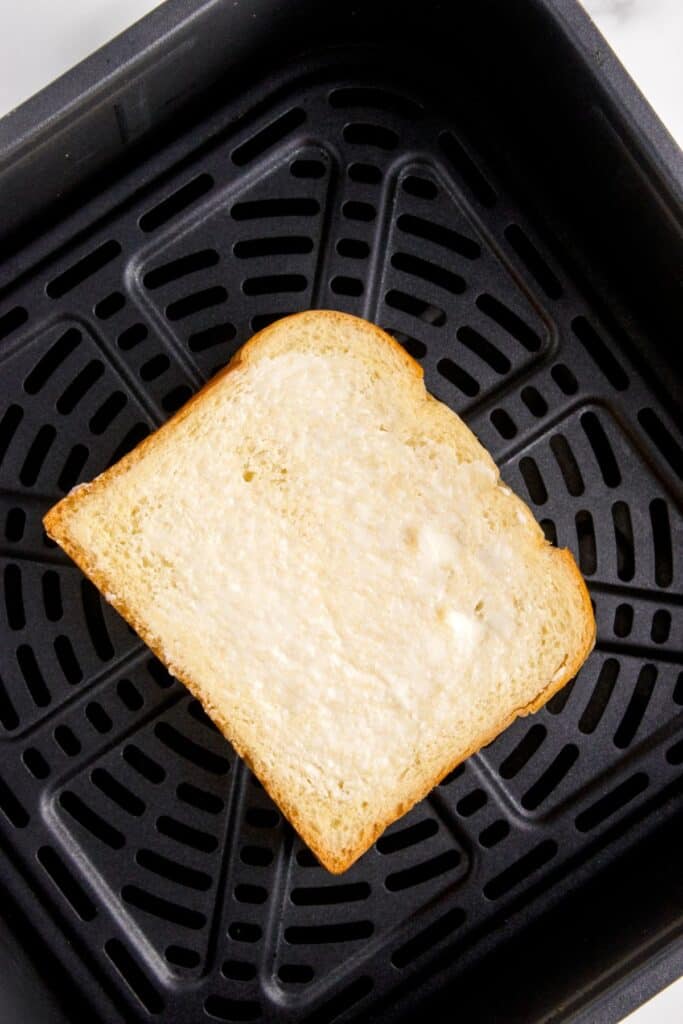 Buttered grilled cheese in an air fryer basket, not cooked yet.