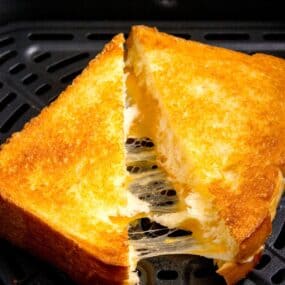 Closeup of grilled cheese in the air fryer basket sliced in half with cheese pulling from both halves.