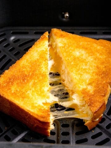 Closeup of grilled cheese in the air fryer basket sliced in half with cheese pulling from both halves.