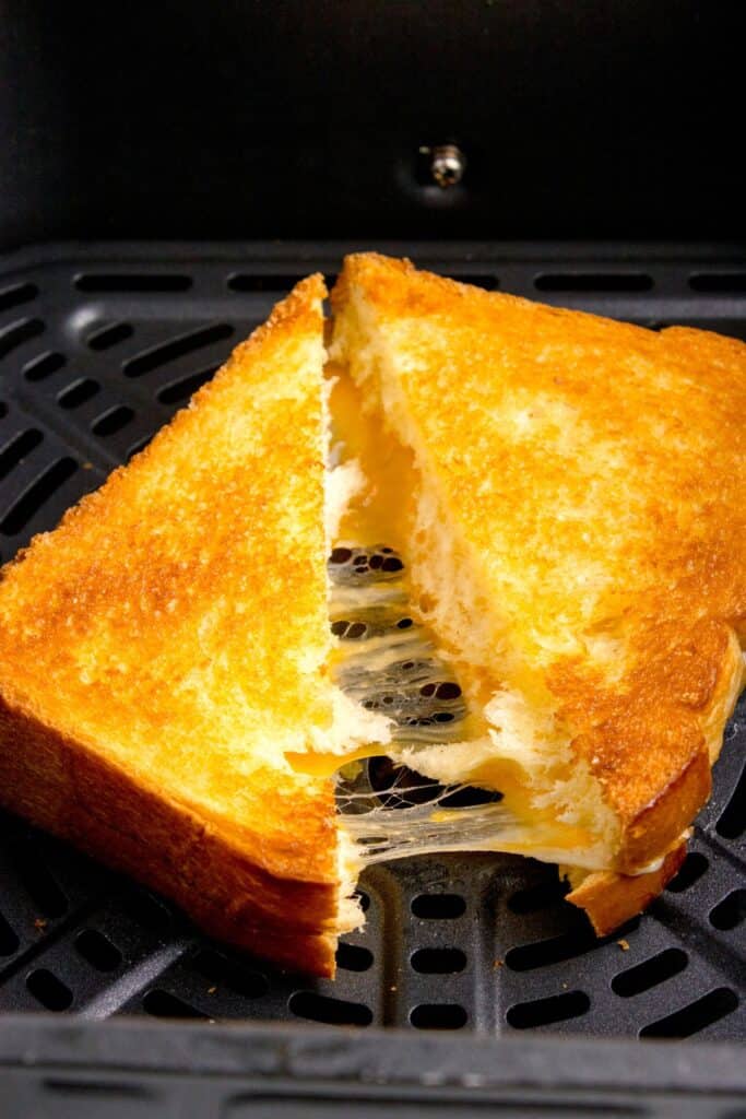 Closeup of grilled cheese in the air fryer basket sliced in half with cheese pulling from both halves.