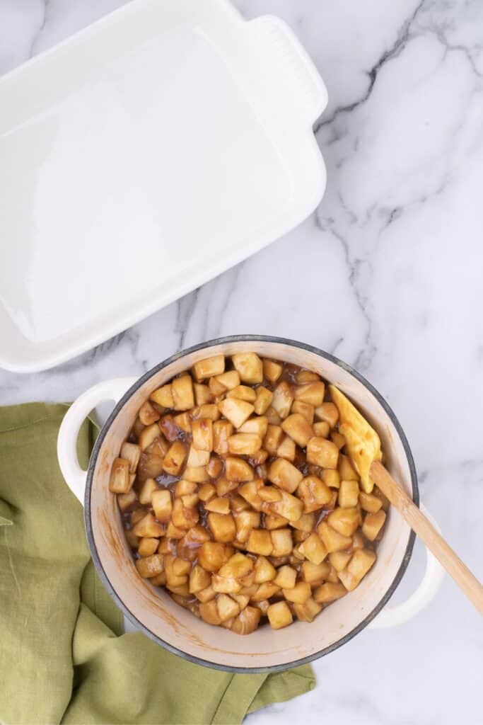 Dutch oven of baked apples next to an empty white baking dish.