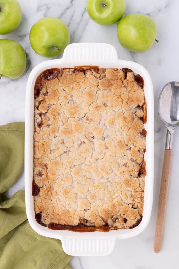 Overhead image of baked apple cobbler surrounded by green apples and a serving spoon.