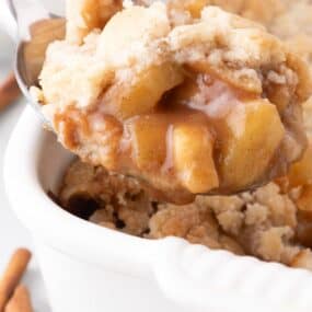 Close up of serving spoon lifting apple cobbler out of the baking dish.