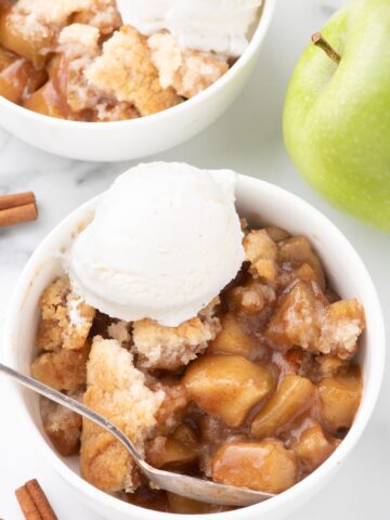 Overhead image of two bowls of apple cobbler with ice cream on top.