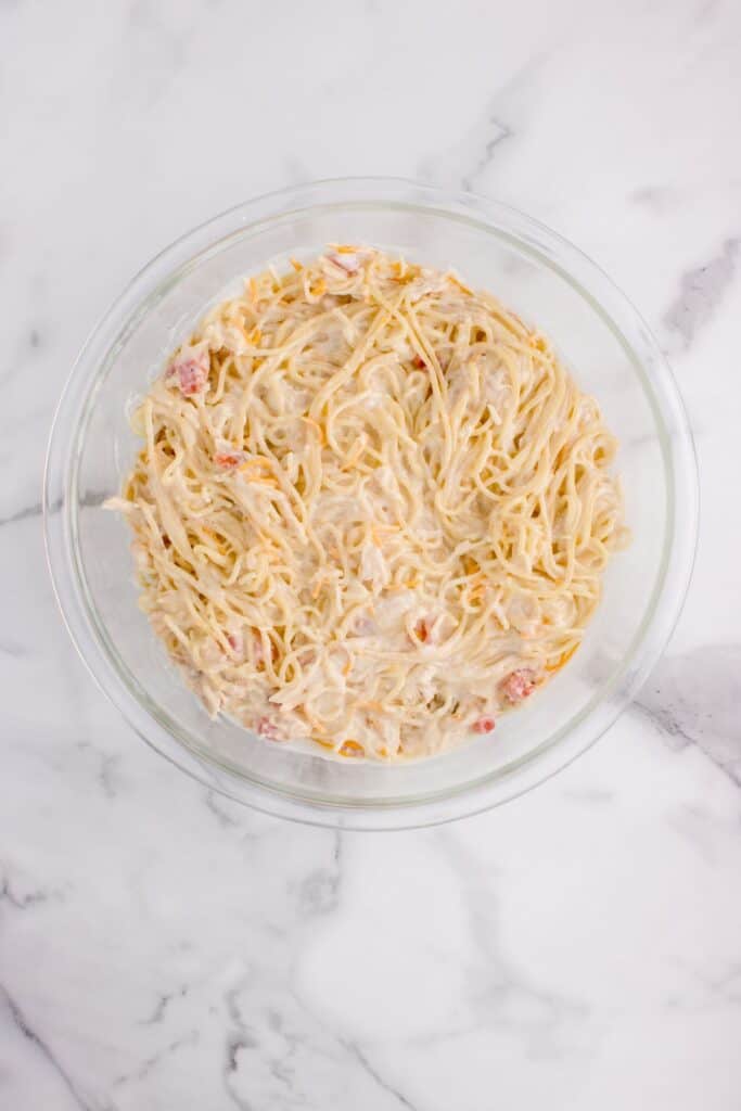 Bowl of shredded chicken, heavy cream, Rotel, cheese, cream of chicken soup, and spaghetti for chicken tetrazzini recipe.