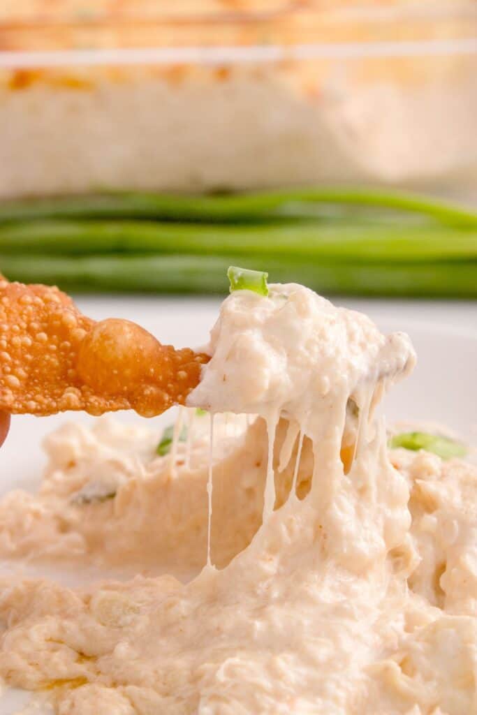 Crab rangoon dip on a white dish with a wonton chip dipped in it.