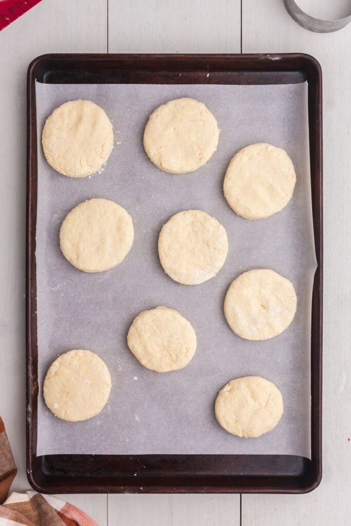 Baking sheet lined with parchment paper. Cut circles of biscuit dough placed on top of parchment.