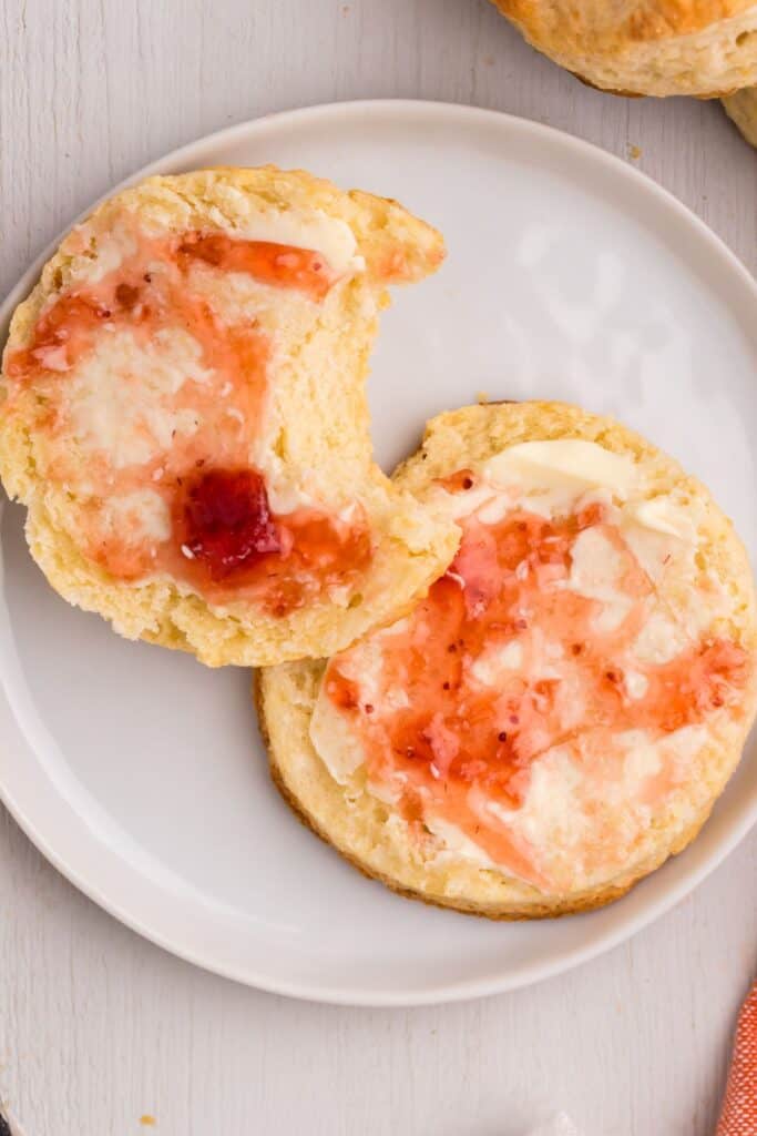 White plate with halved biscuit smeared with butter and strawberry jam.