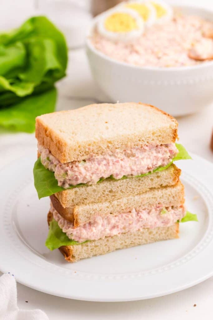 Ham salad in a sandwich. Sandwich is sliced in half. One half is on top of the other on a white plate.