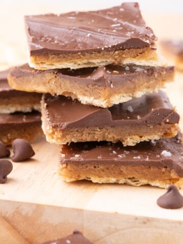 Saltine cracker toffee stacked on a cutting board with chocolate chips.