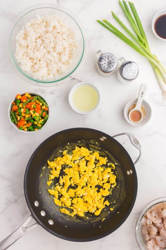 Shrimp fried rice ingredients around a skillet scrambling eggs.