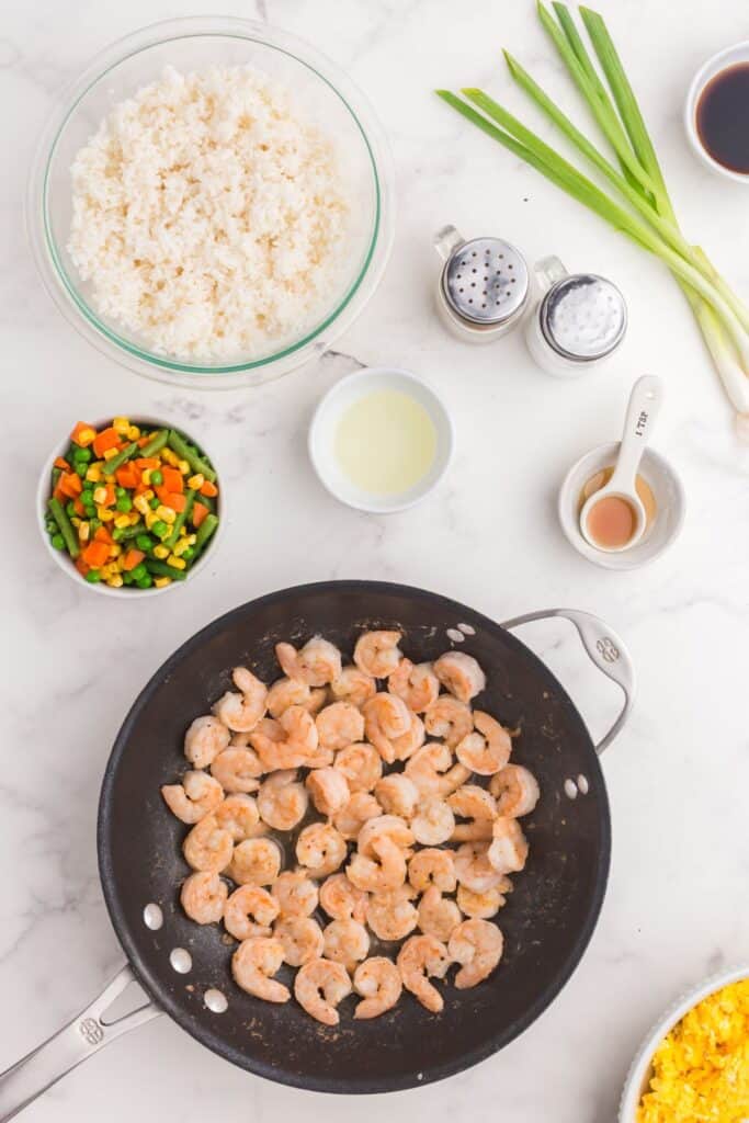 Shrimp fried rice ingredients around a skillet with cooked shrimp.