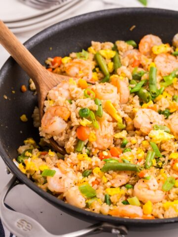 Close up view of a skillet with shrimp fried rice. A wooden spoon is stirring the fried rice recipe.