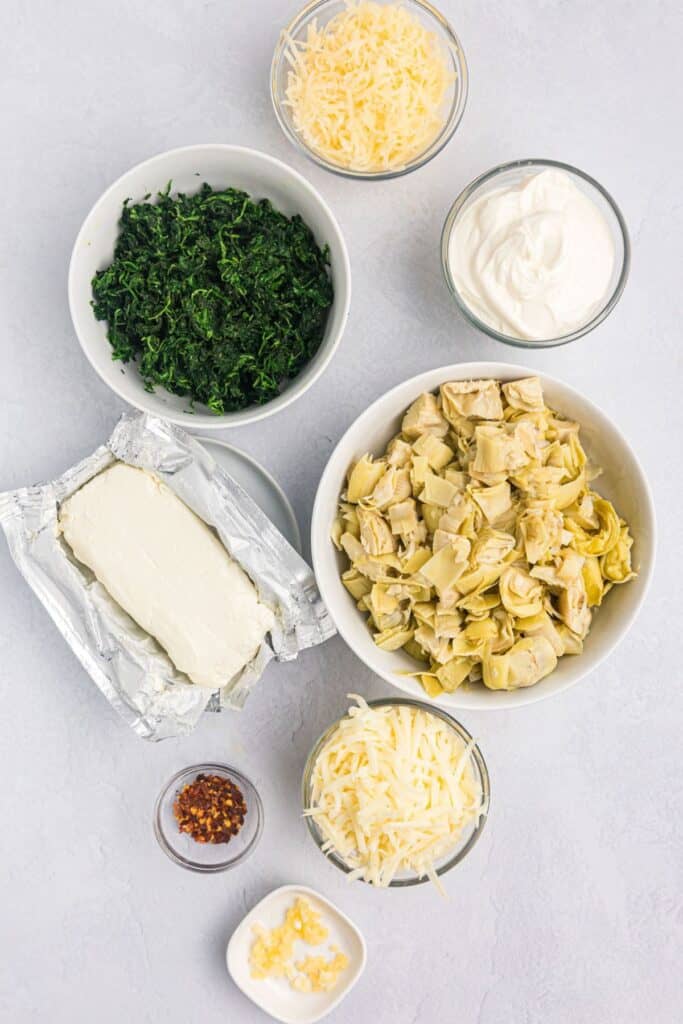 Ingredients for Spinach Artichoke Dip: cream cheese, sour cream, garlic, mozzarella, parmesan, red pepper flakes, artichoke hearts, frozen spinach