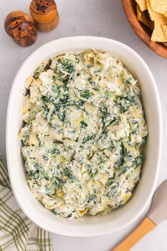 Spinach artichoke dip unbaked in a white serving bowl.