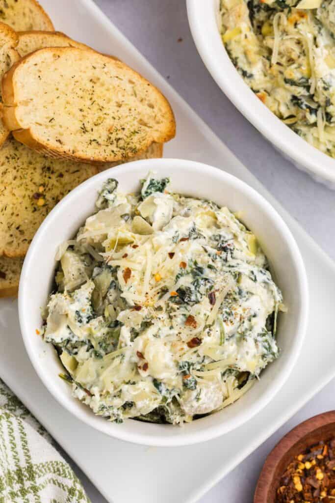 spinach and artichoke dip in a serving bowl with crustini around it.