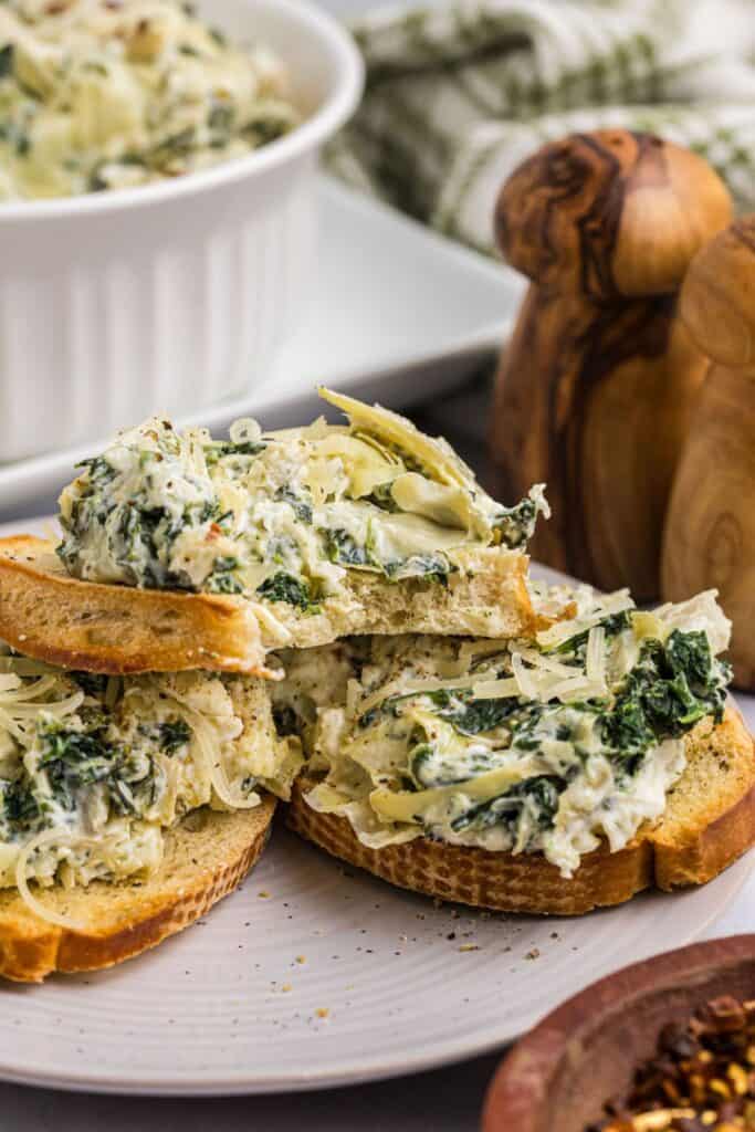 Crustini with spinach and artichoke dip spread on them on a serving plate.