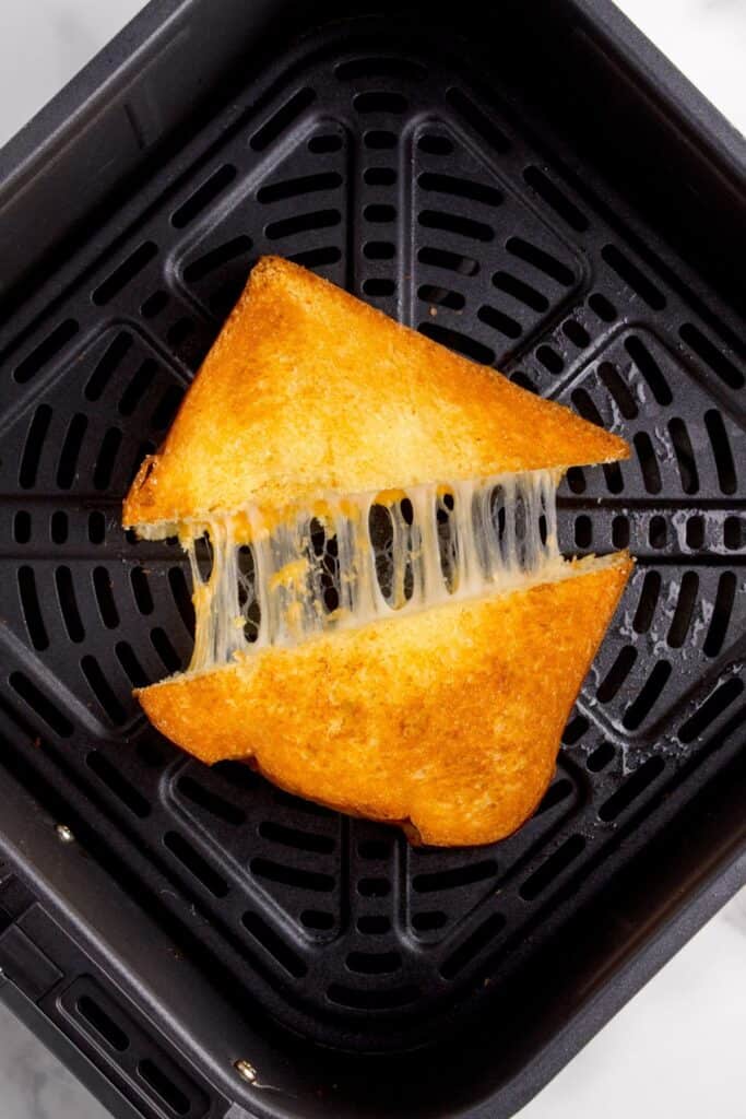 air fryer grilled cheese in the air fryer basket cut in half with cheese pulling between the two halves.