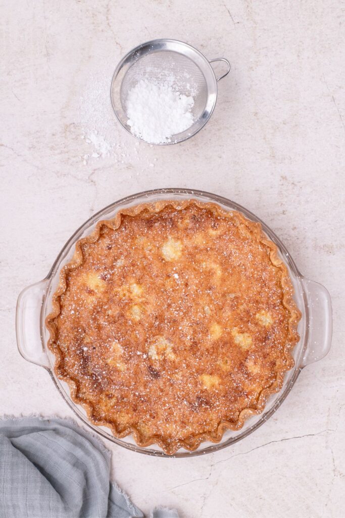 Overhead view of chess pie and a sifter with powdered sugar in it.