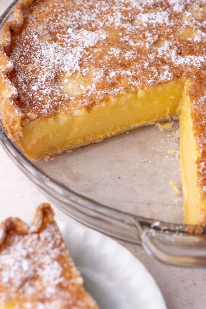 Overhead image of a sliced chess pie. Slice of pie on a white serving dish is next to the pie plate.