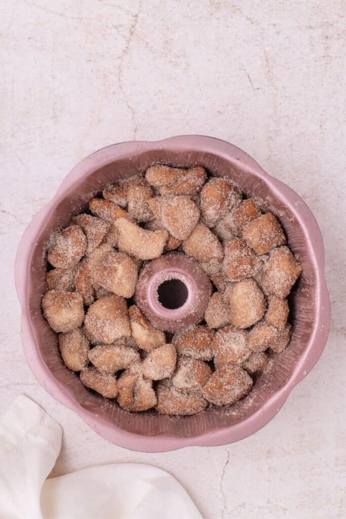 Biscuit dough chopped and rolled in sugar. Raw biscuit pieces are placed in a bundt pan.