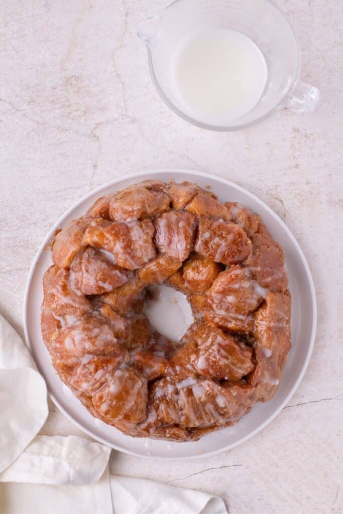 Over head view of monkey bread with icing on it. Above the bread is a measuring cup with extra icing.