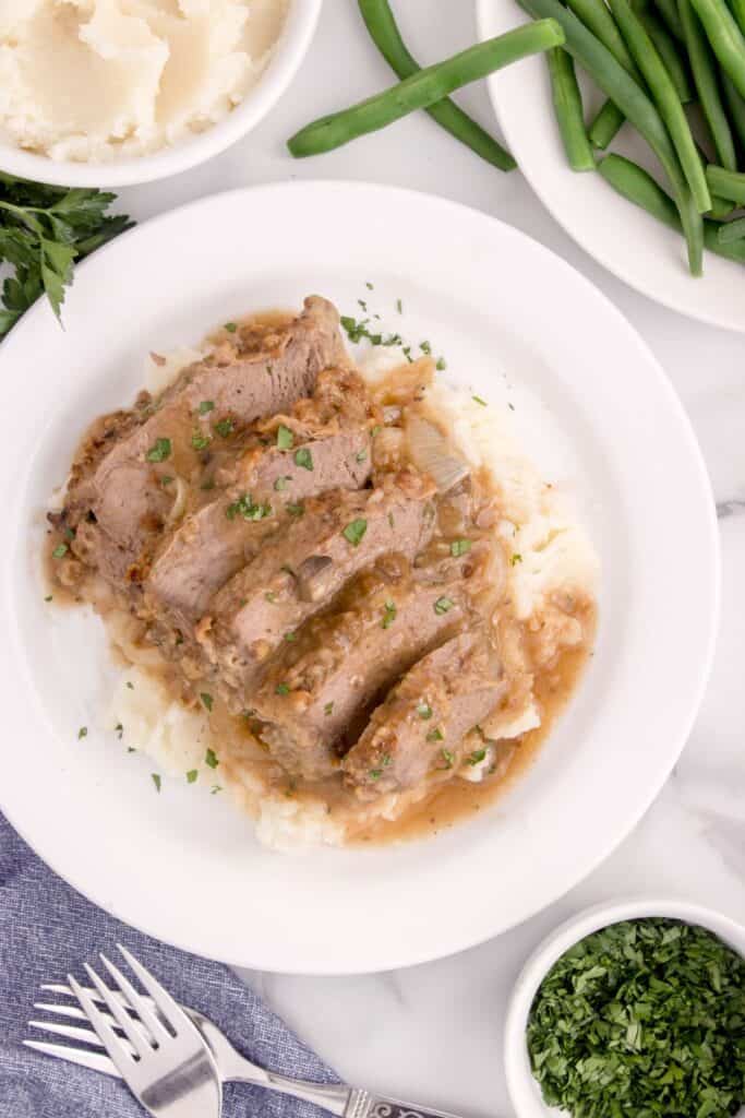 Overhead view of a white dinner plate with mashed potatoes and round steak. The dish is drizzled with gravy.