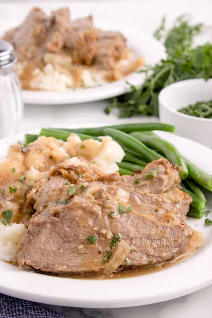 Round steak on a white dinner plate with mashed potatoes, green beans, and gravy.