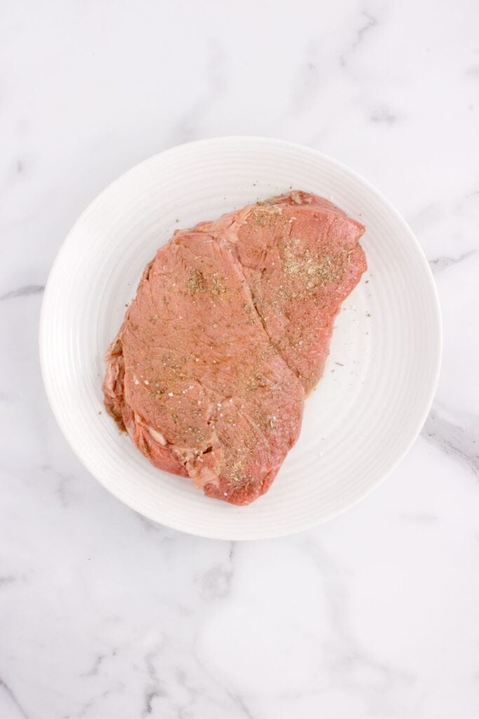 Round steak seasoned on a white dinner plate.